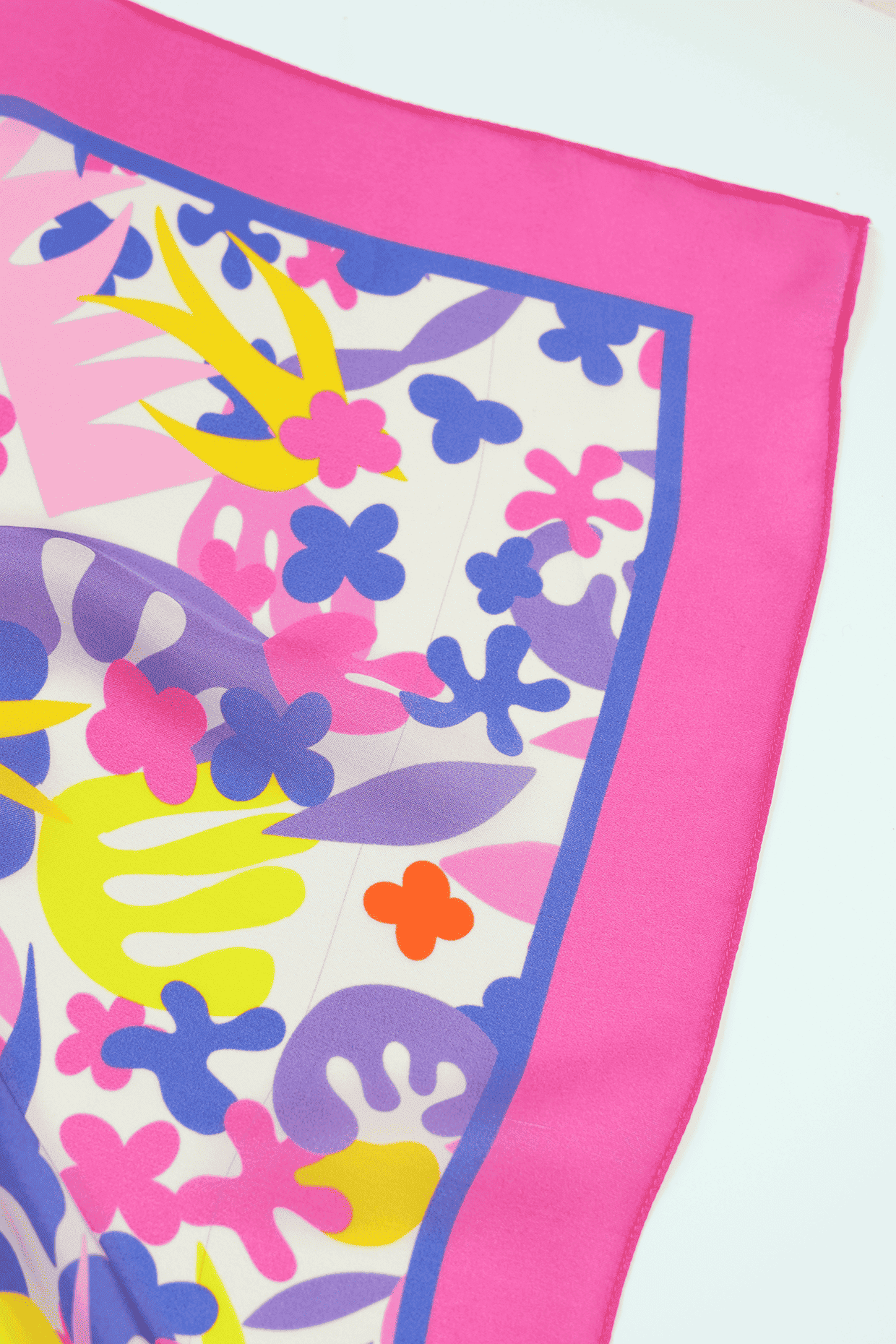 Colorful floral patterned scarf corner with pink border on a white background
